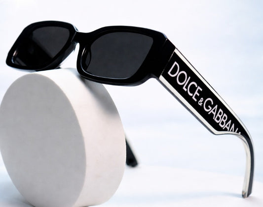 Sunglasses feature a chunky black rectangular acetate frame with a prominent white logo printed on the wide temples