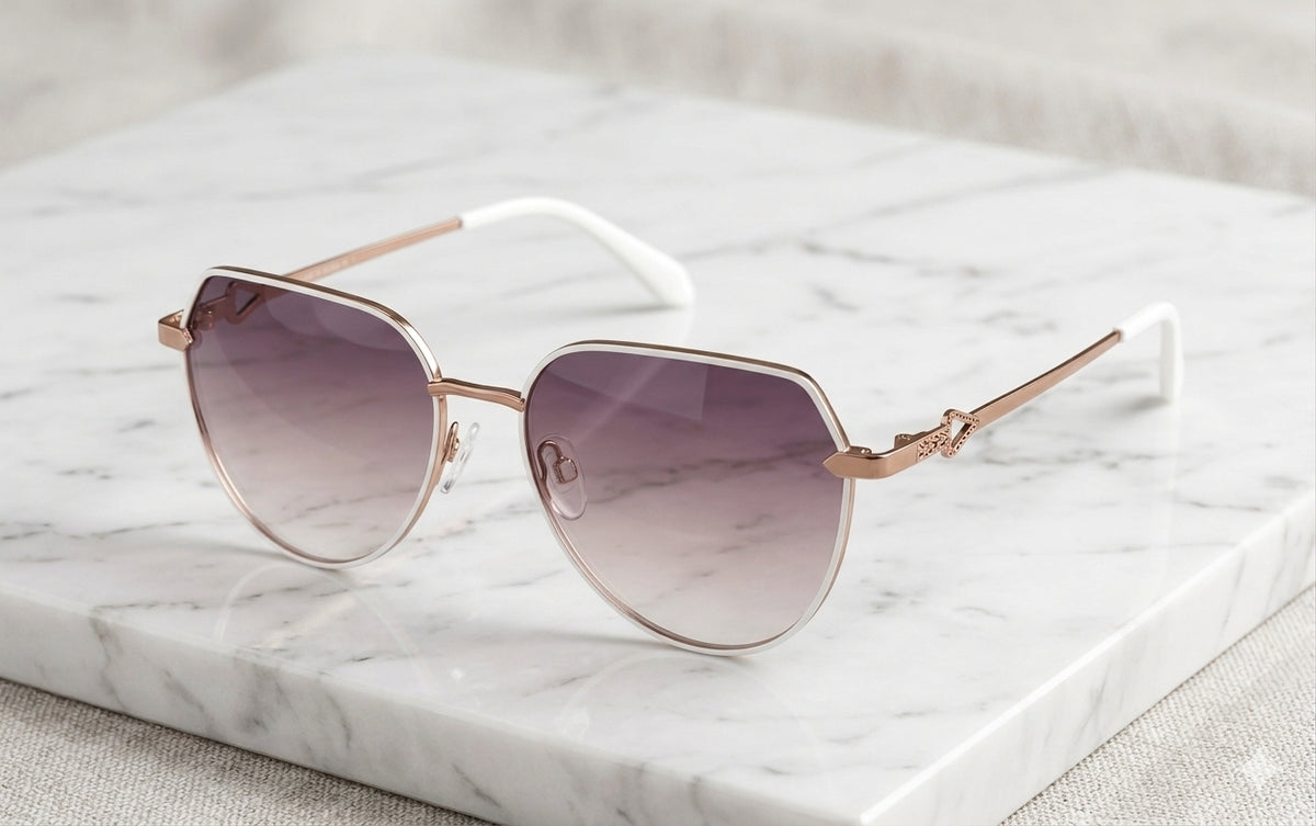 A pair of oversized shield-style sunglasses with rose gold metal frames and gradient purple lenses, resting on a white marble block.